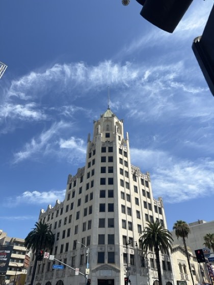A white Art Deco tower on a street corner, wispy cirrus across a deep blue sky, palms below.
